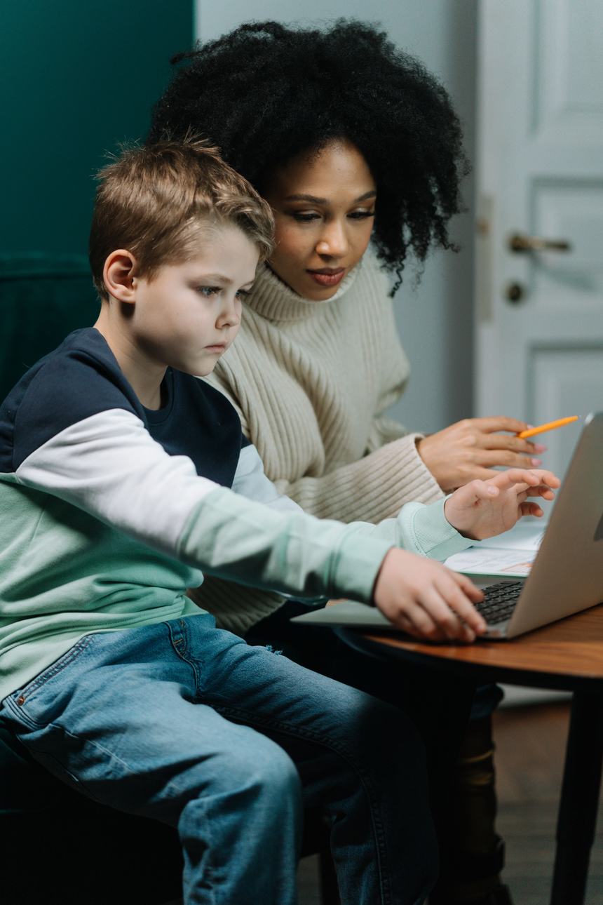 An adult helps a boy with homework on a laptop at home